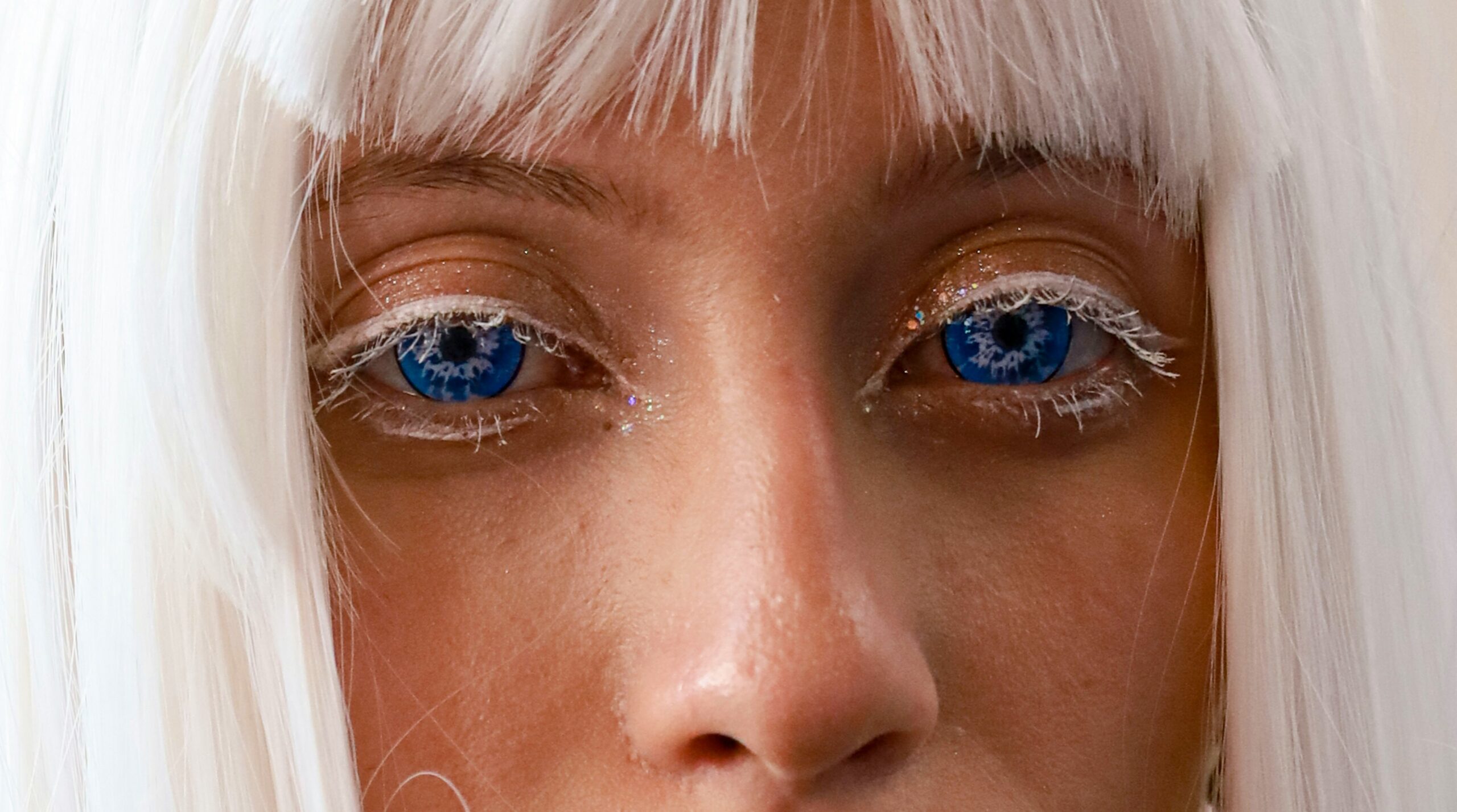 A model wearing striking blue eyeshadow with geometric lines on her cheeks